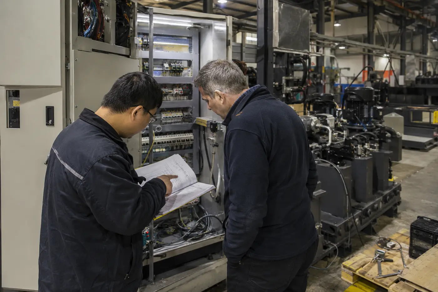 Illustrative factory engineer and sourcing inspector reviewing industrial machinery